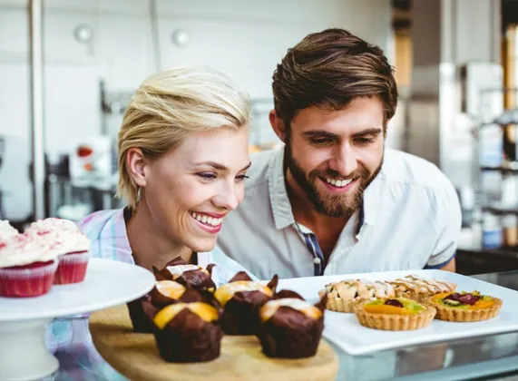 Customers choosing muffins and tarts at a bakery counter